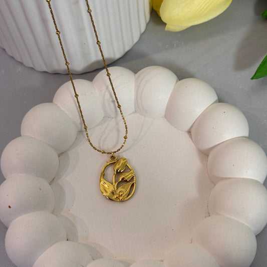White beaded bracelet with a gold charm on a white surface with a yellow flower.