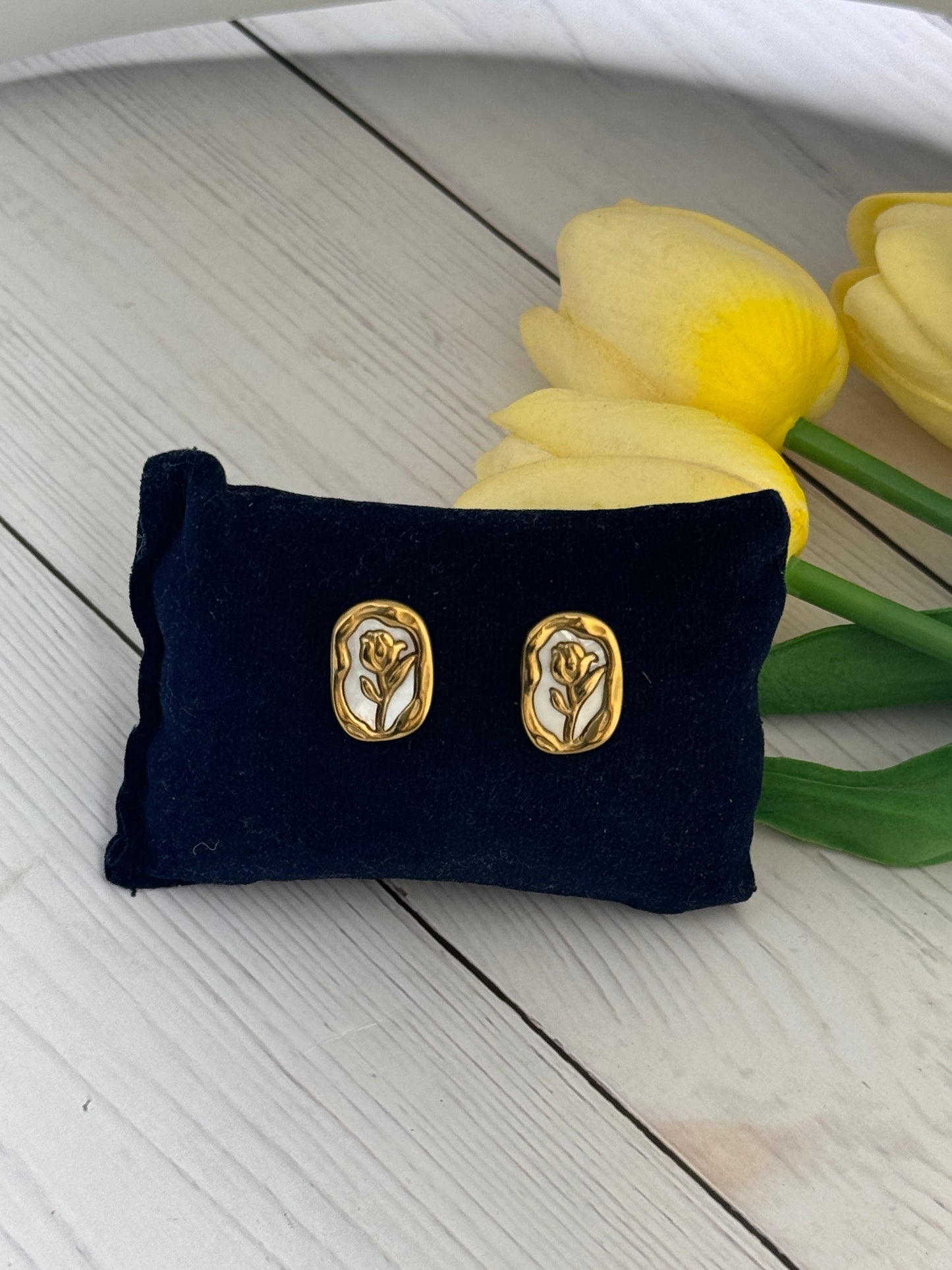 Gold earrings on a black pillow with yellow tulips in the background
