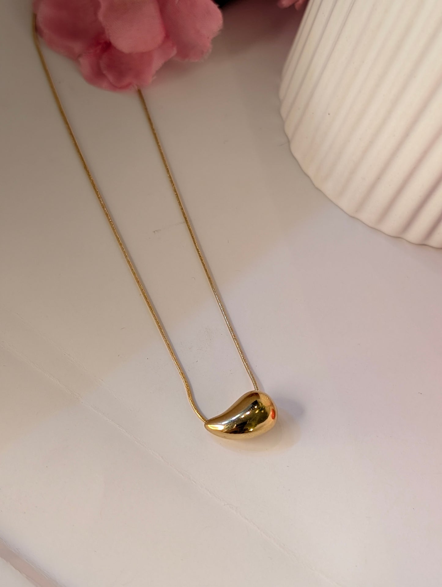 Gold necklace on a white surface with a pink flower in the background