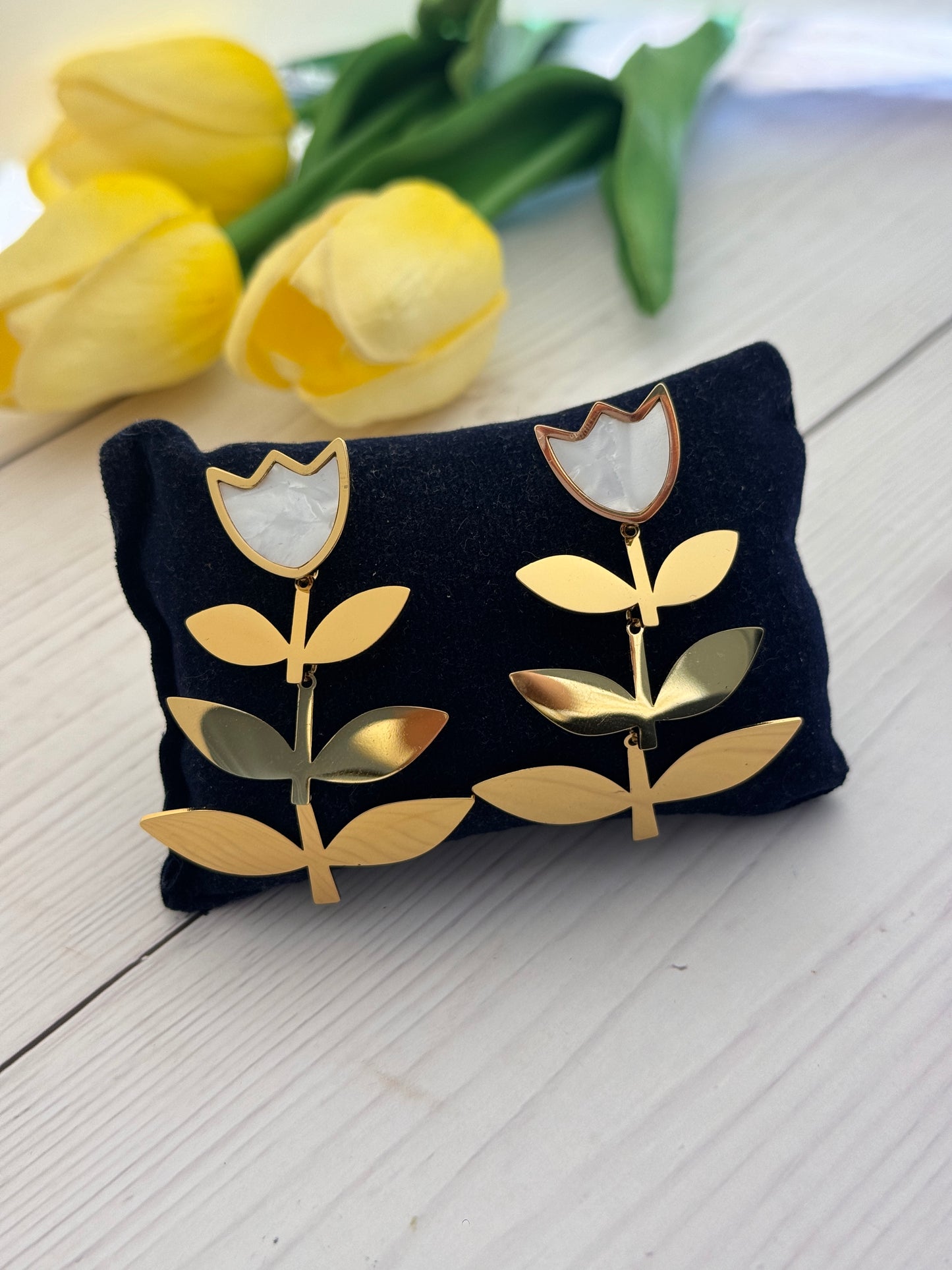 Black jewelry pillow with gold leaf design on a wooden surface with yellow tulips.