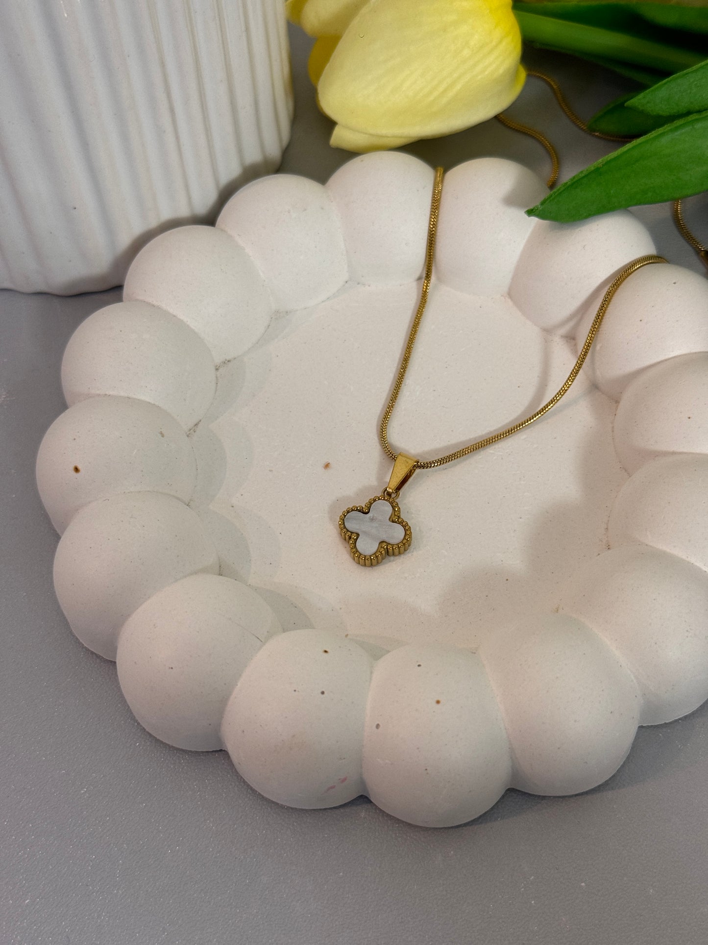 Necklace with a clover pendant on a white stone surface next to a yellow tulip.
