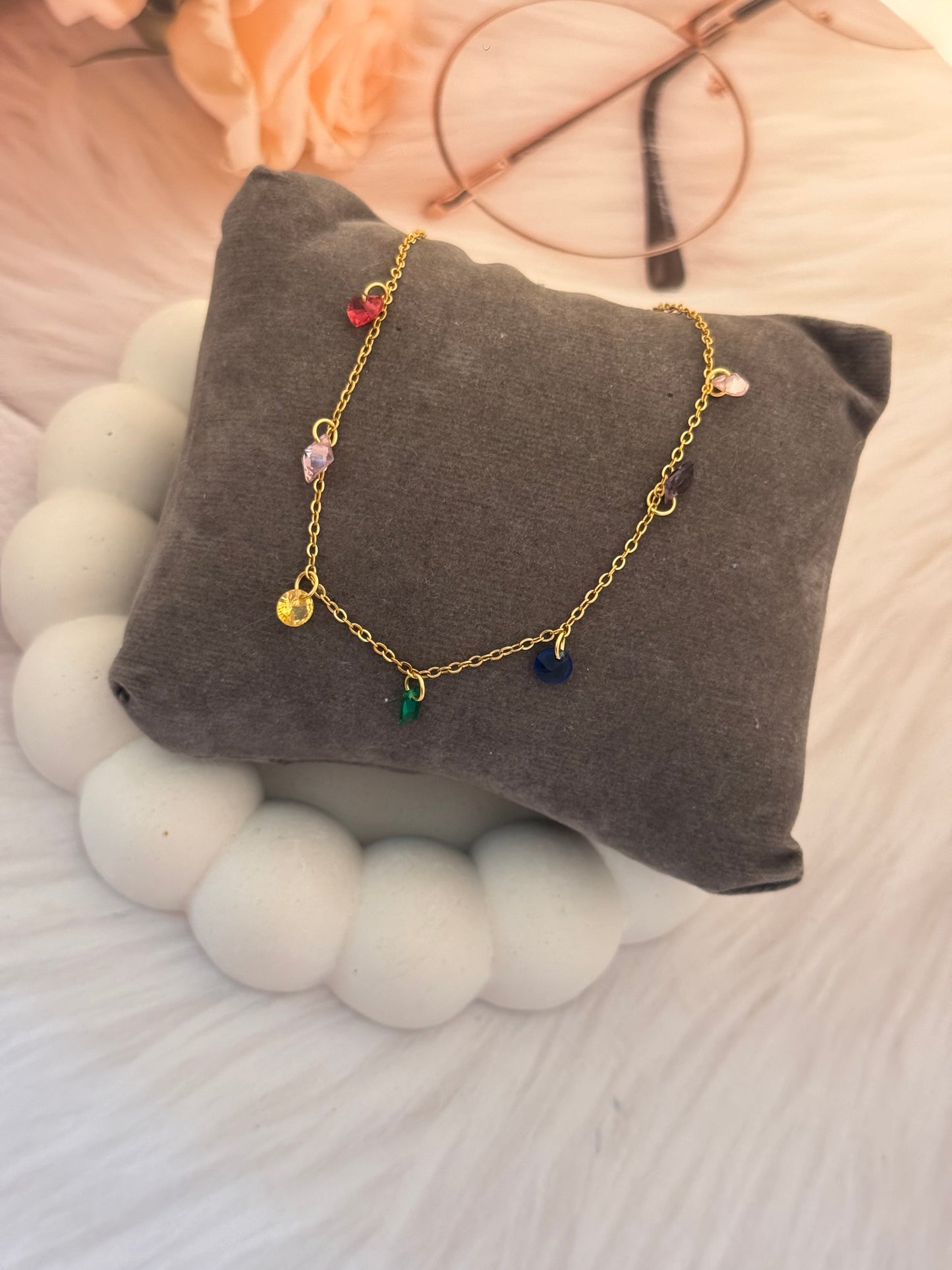 Gold bracelet with colorful beads on a gray pillow surrounded by decorative items.