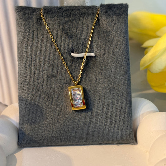 Gold necklace with a pendant on a gray textured stand with a blurred background