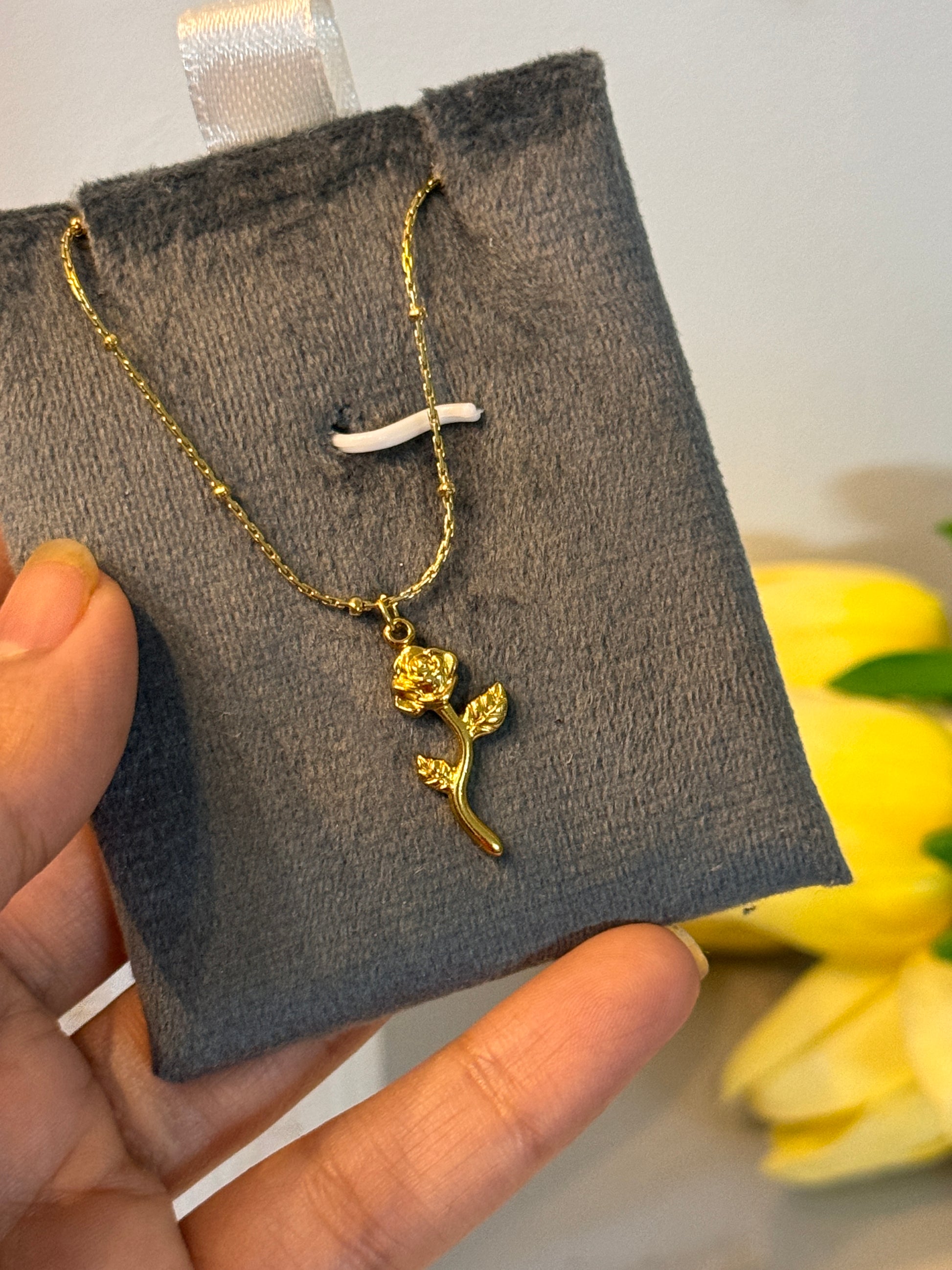Gold necklace with floral design held on a gray jewelry pouch.