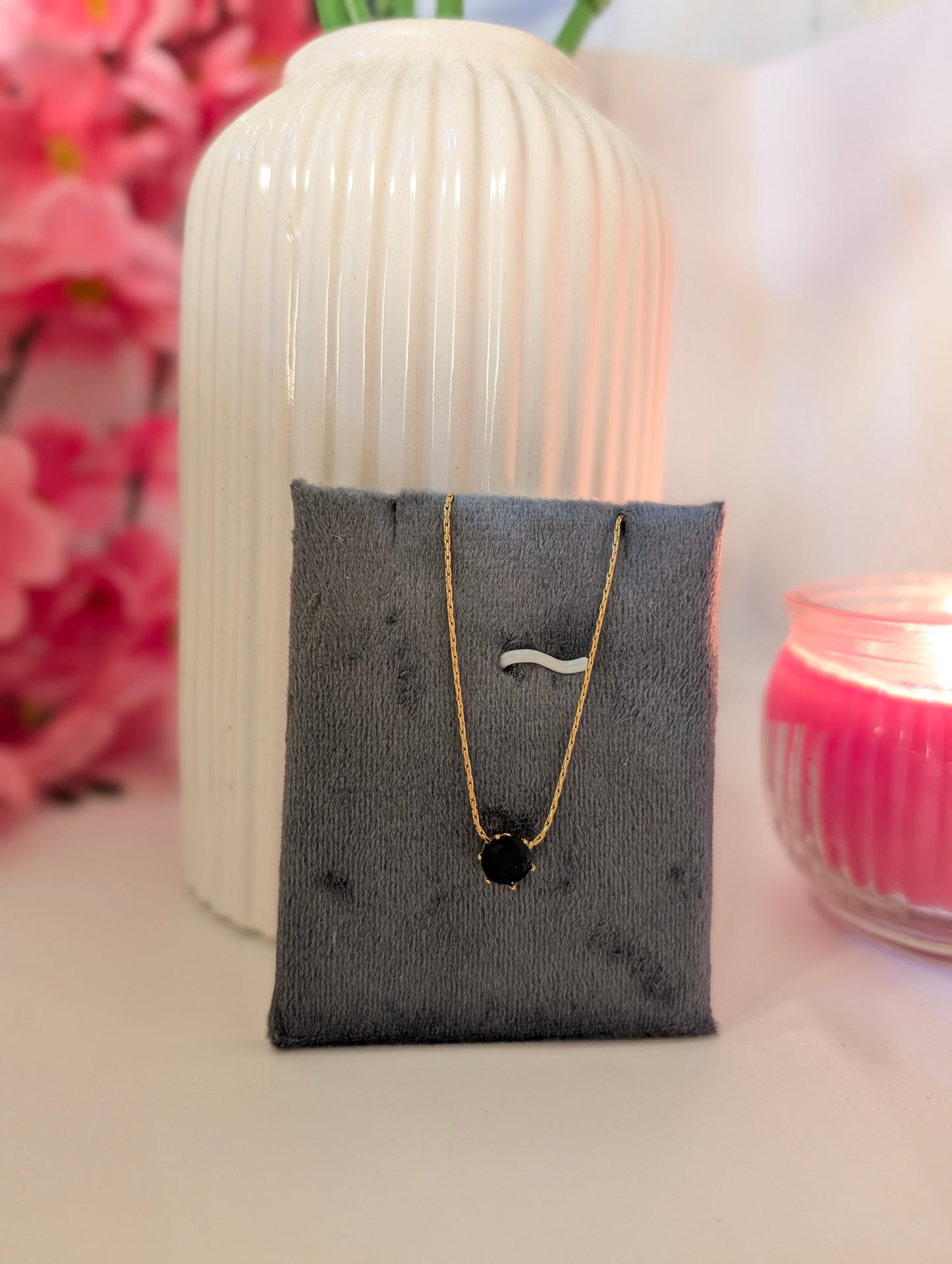 Necklace with a black pendant on a gray display stand against a soft pink background
