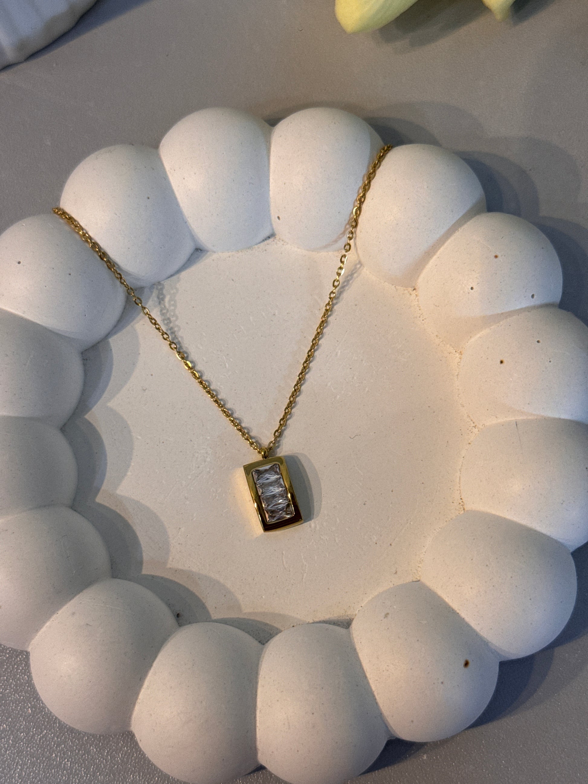 Gold necklace with a pendant on a white stone surface