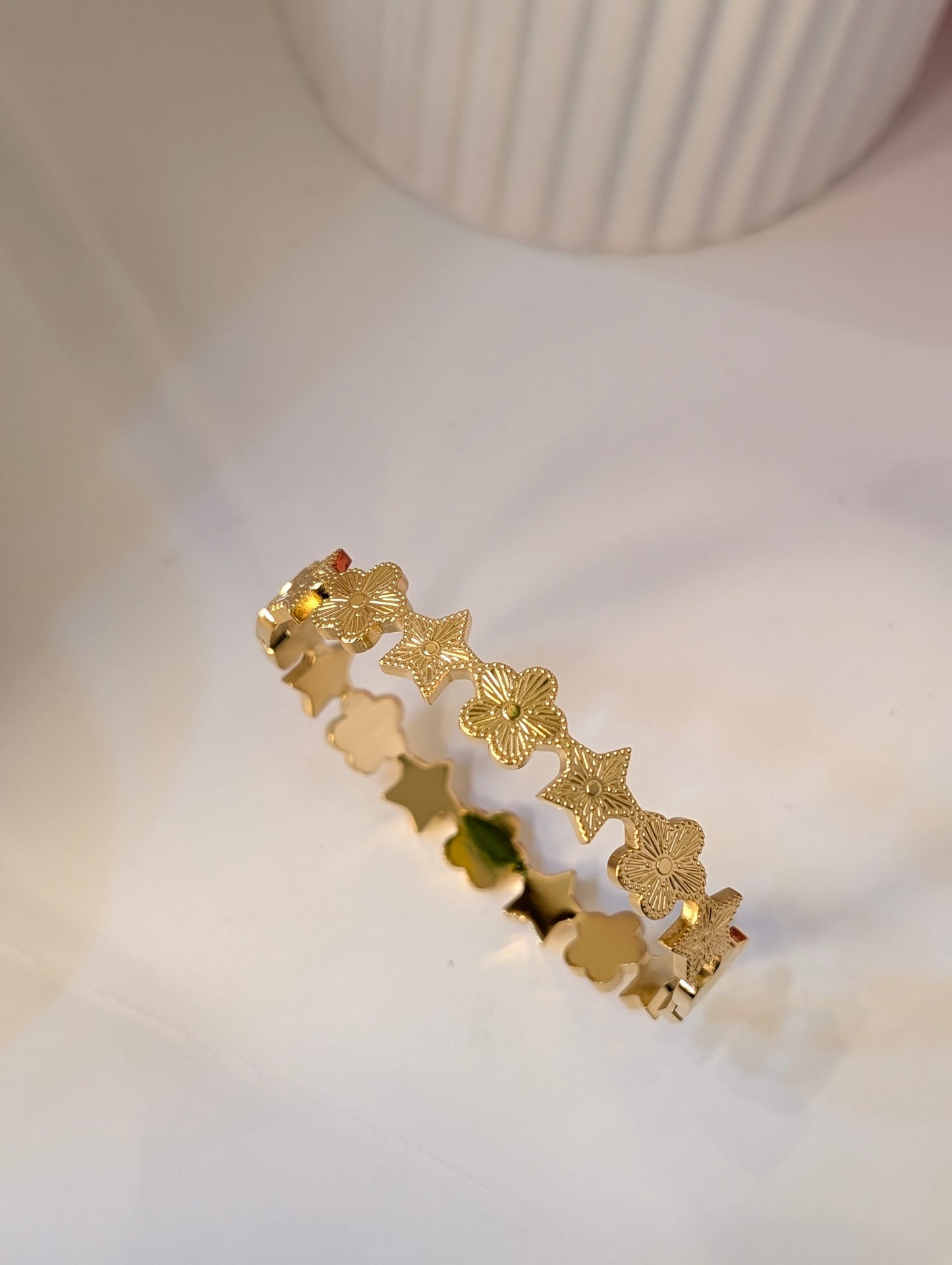 Gold bracelet with star and leaf designs on a white surface