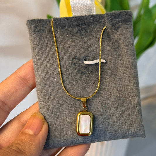Gold necklace with a pendant on a gray jewelry pillow held by a hand.