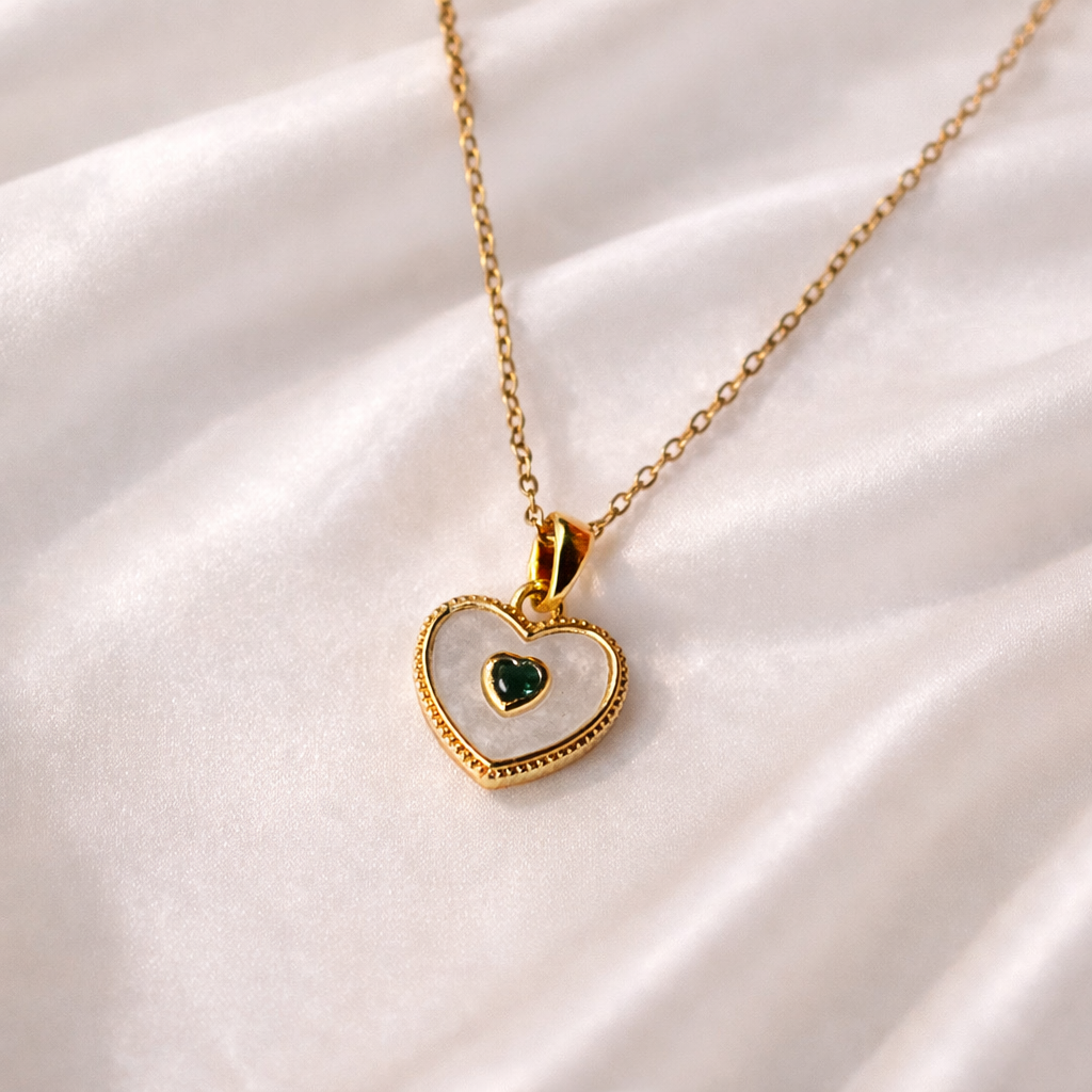 Heart-shaped pendant necklace with a green gemstone on a white satin background