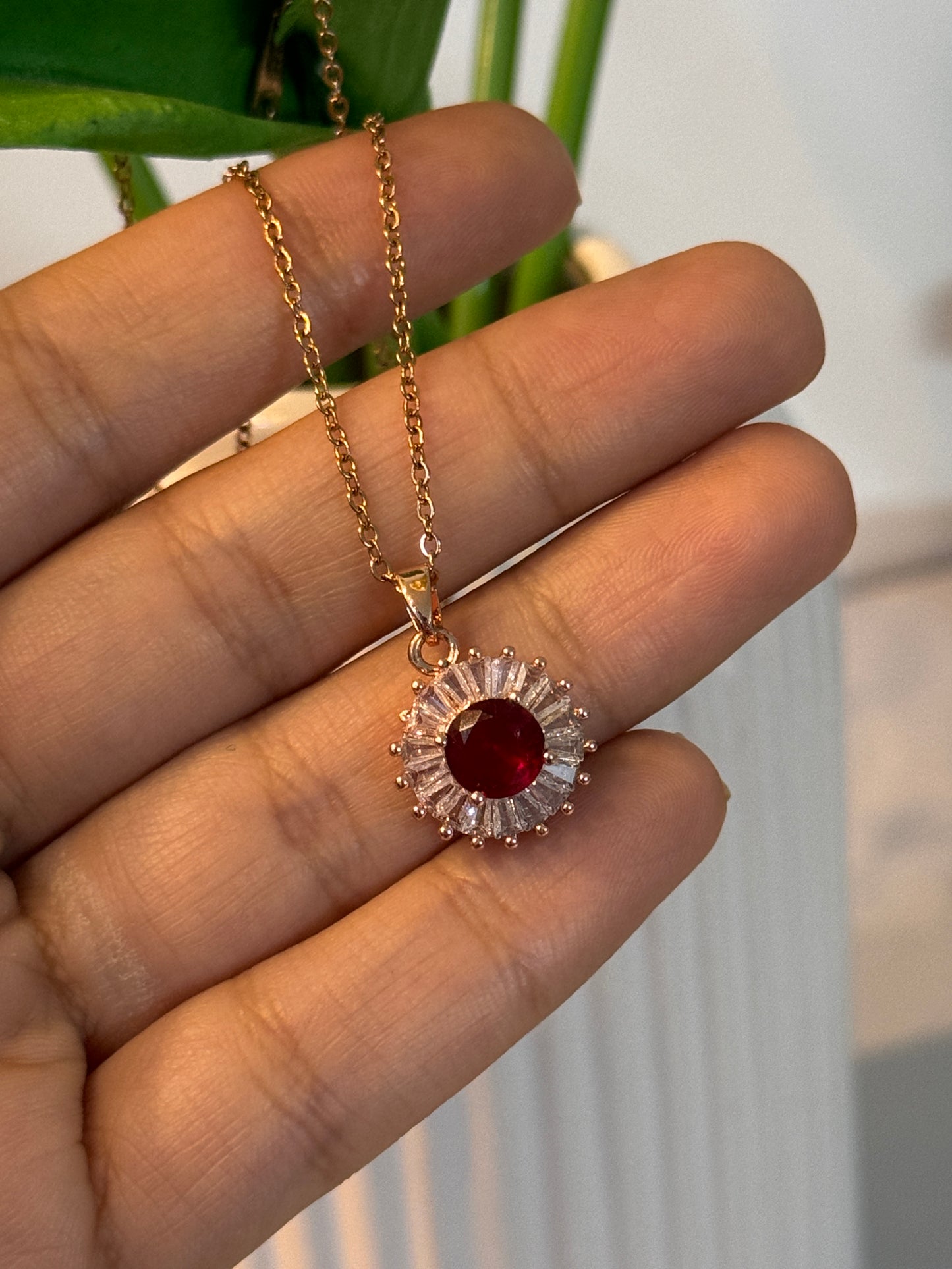 RoseGold necklace with a red gemstone pendant held by a hand against a blurred natural background