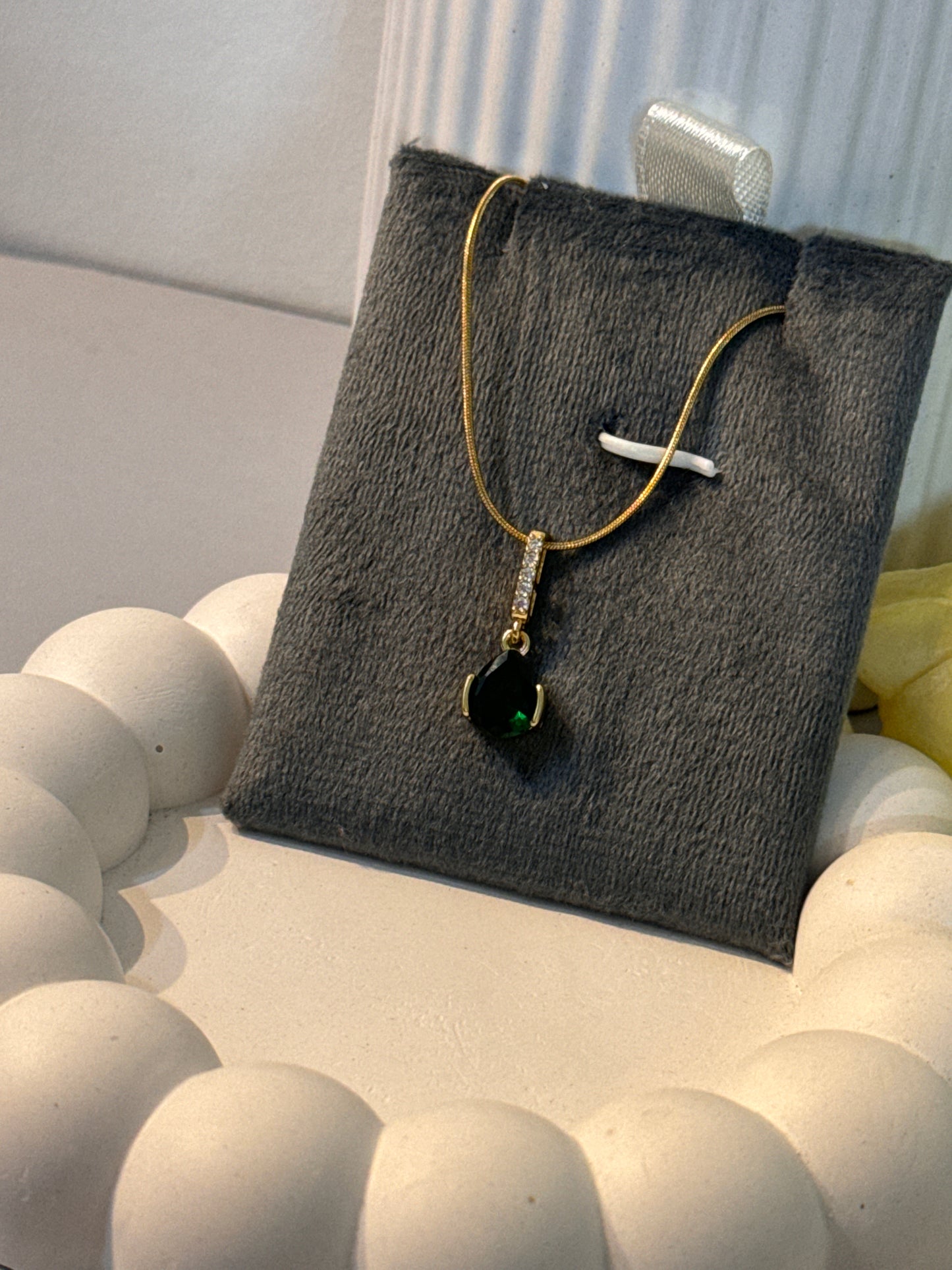 Necklace with a drop-shaped pendant on a gray cushion against a light background