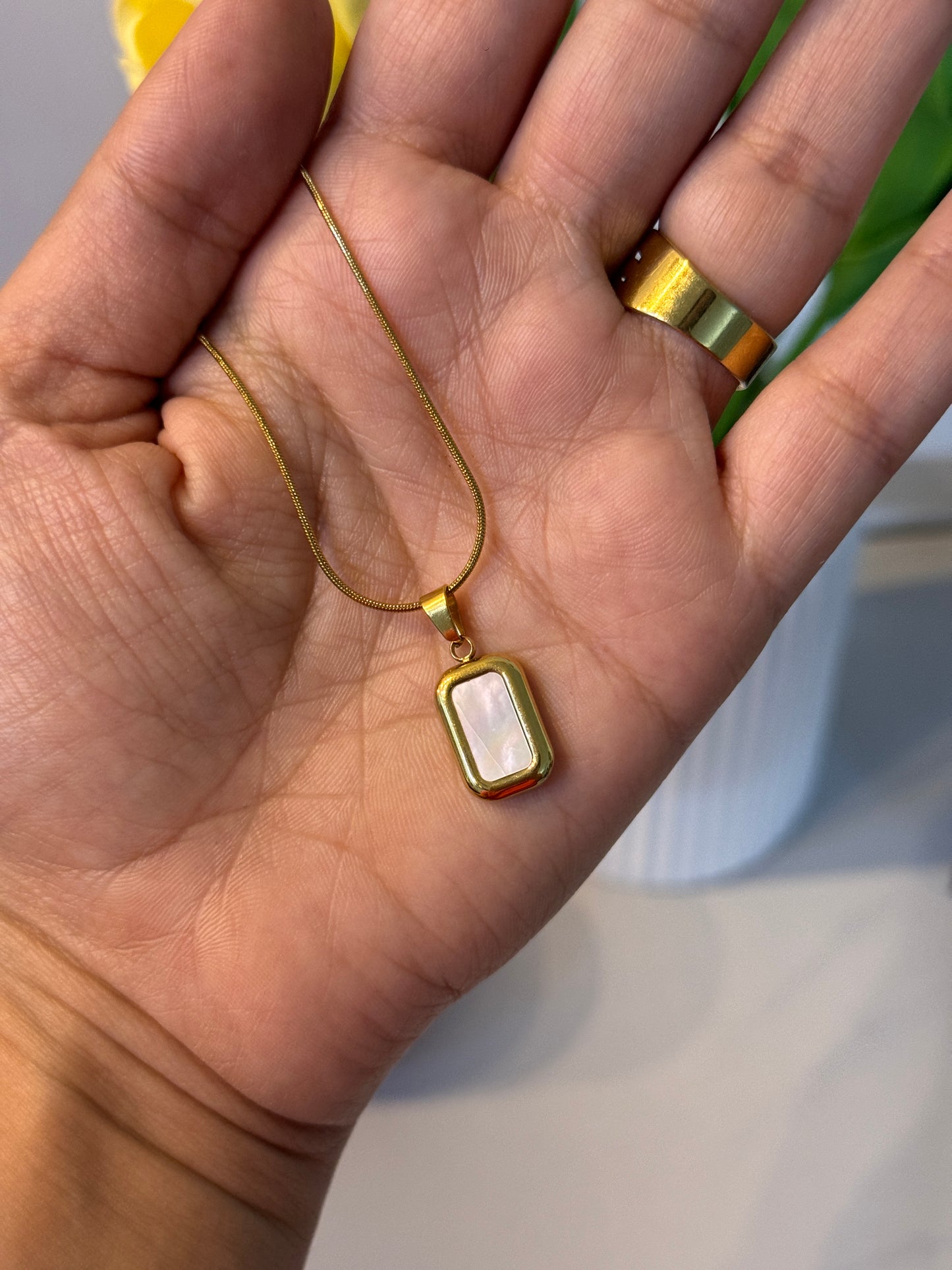 Gold necklace with a pendant held in a hand against a blurred background