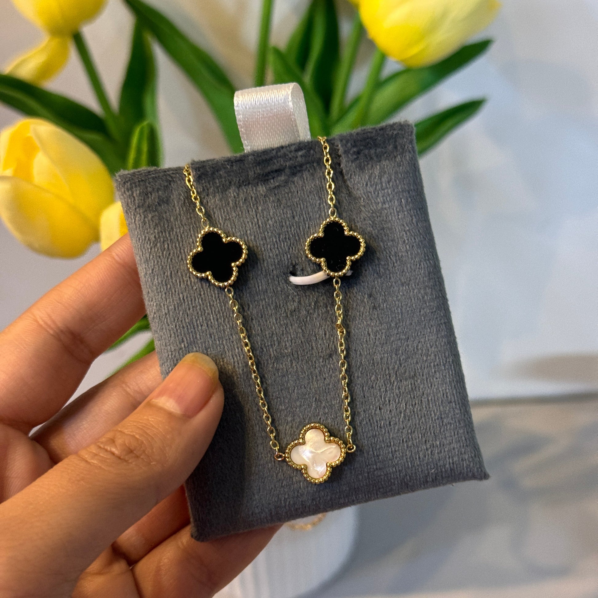 Hand holding a jewelry box with gold and black clover-shaped earrings, yellow tulips in the background