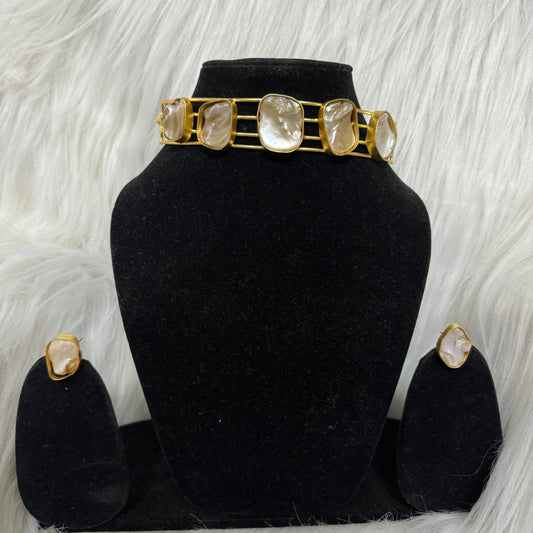 A choker necklace with gold-colored metal and adorned with small, possibly amethyst, stones displayed on a black stand with a white furry background.