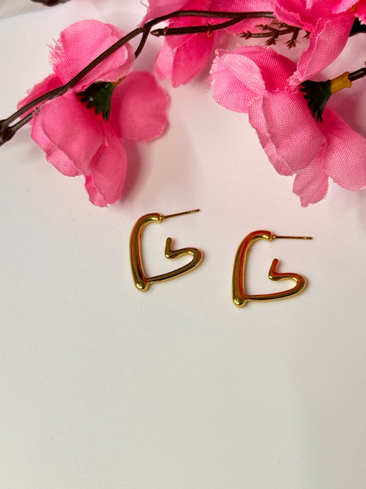 A pair of gold-colored hoop earrings with an open heart design, displayed against a white background with pink floral accents.