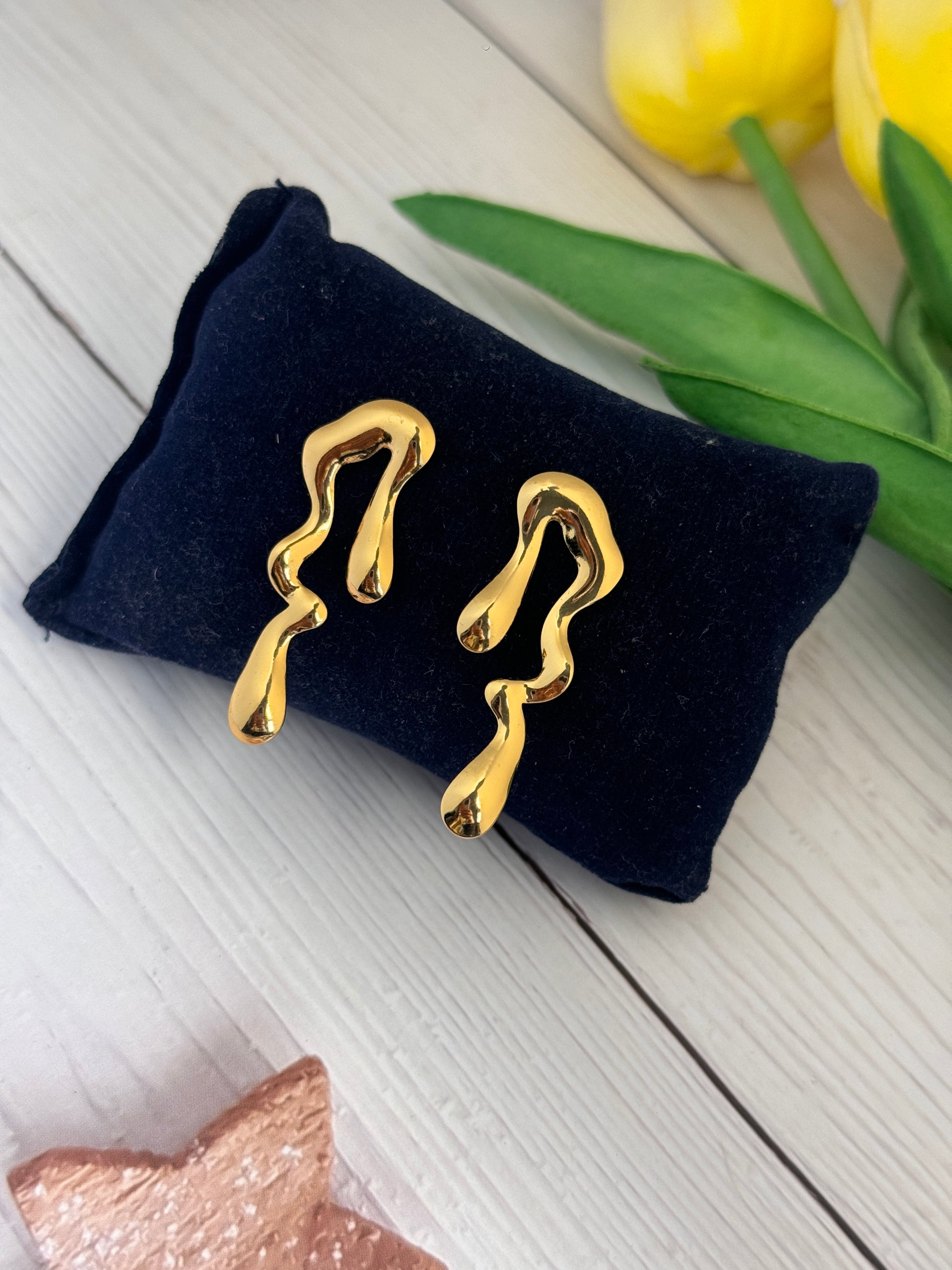 Gold earrings on a black velvet stand with yellow tulips in the background