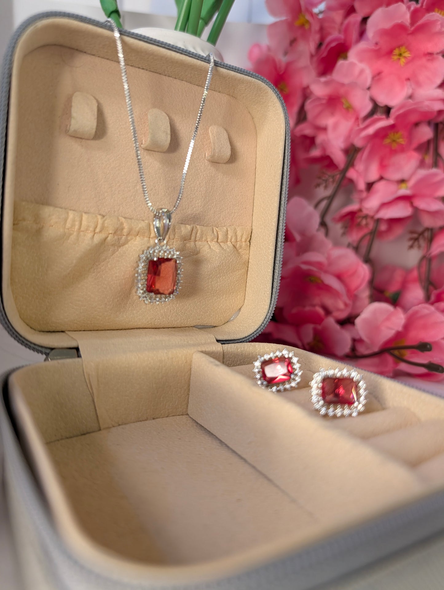 Jewelry set with red gemstones in a beige jewelry box with pink flowers in the background