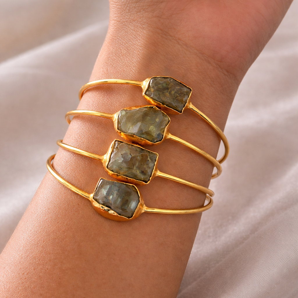 Gold bracelet with green stones on a wrist against a neutral background