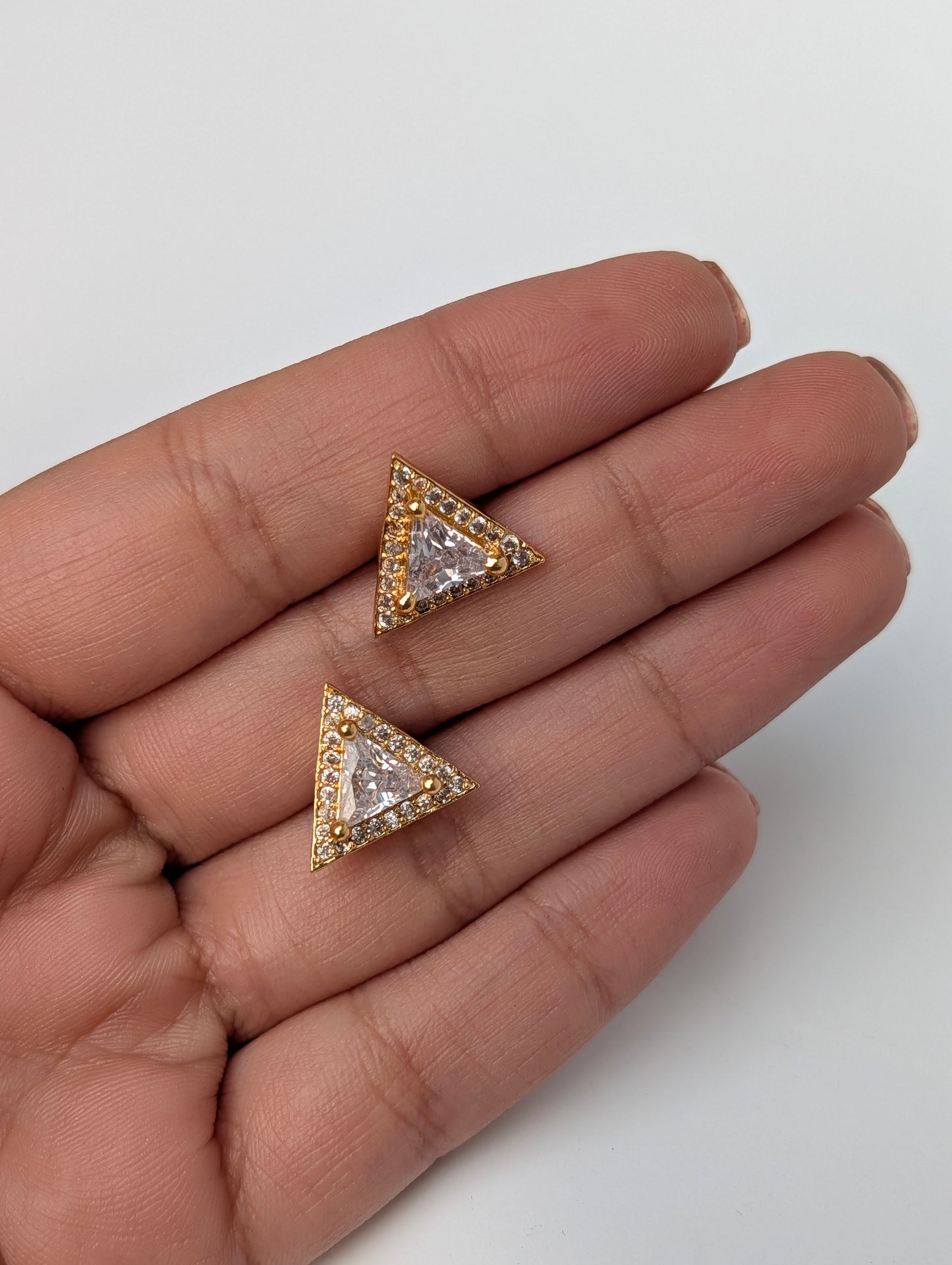 Two triangle-shaped earrings held between fingers on a white background