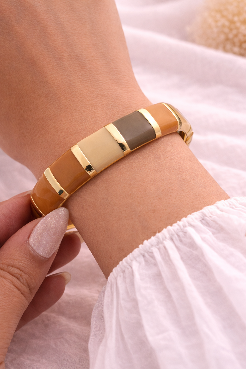 Bracelet with gold and brown bands on a wrist against a light background