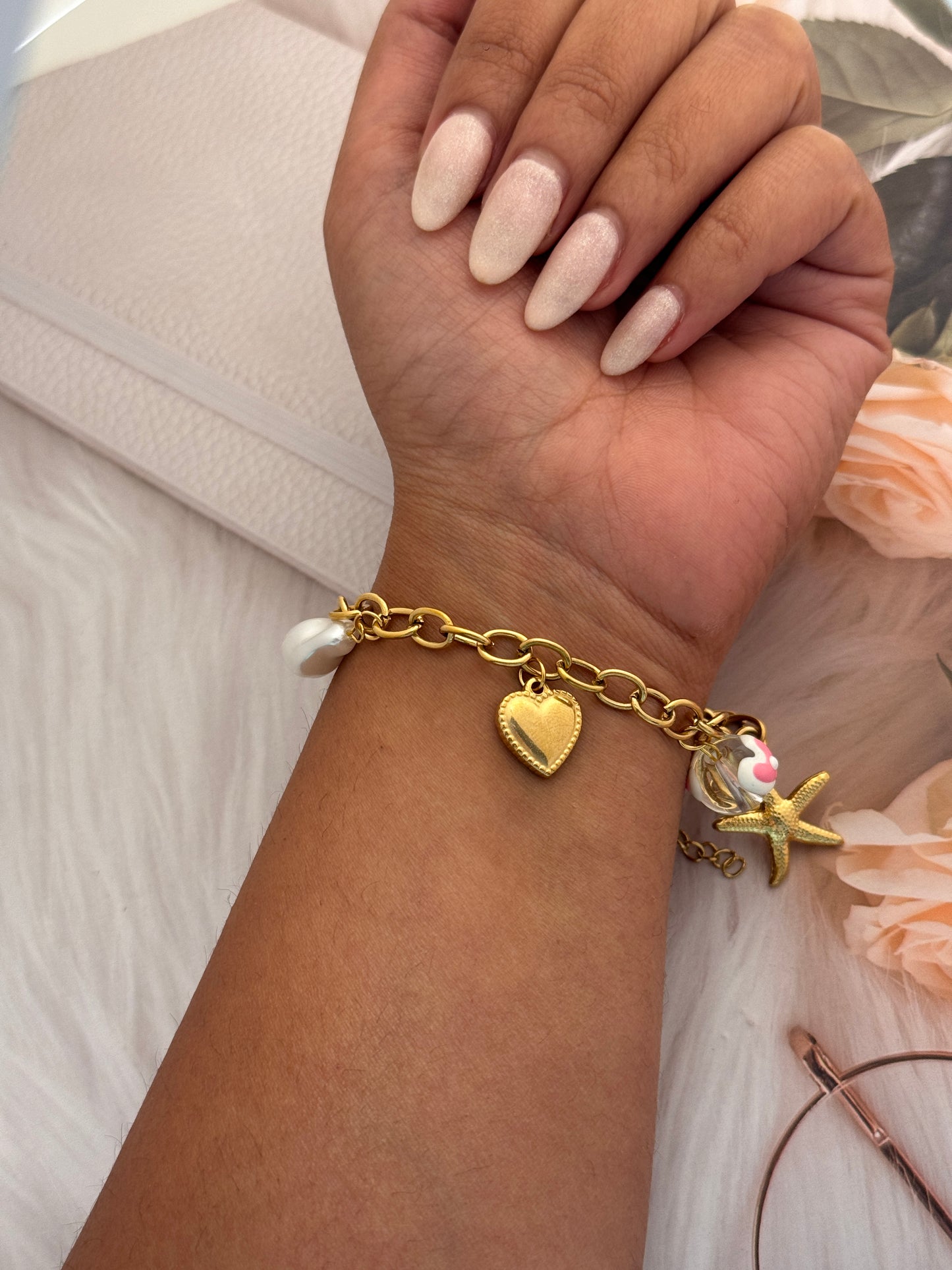 Gold bracelet with charms on a wrist against a neutral background