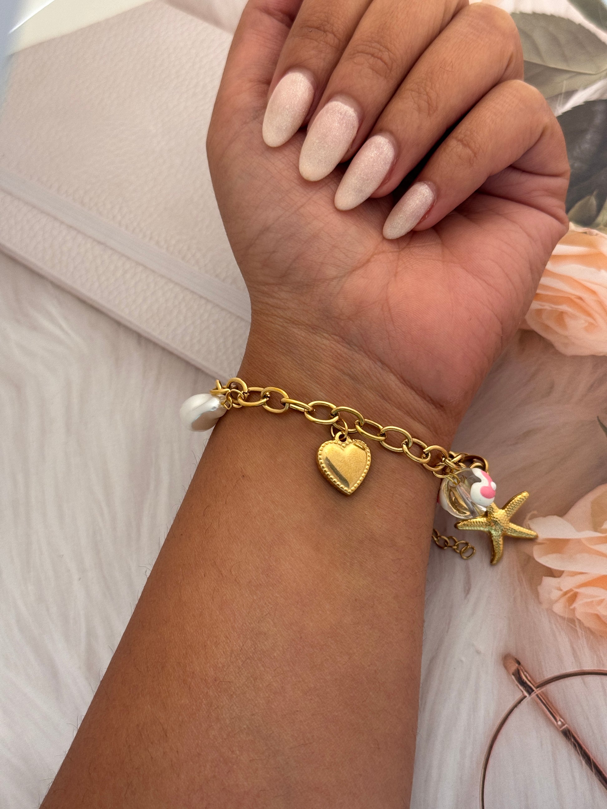 Gold bracelet with charms on a wrist against a neutral background
