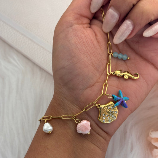 Gold bracelet with various charms on a wrist against a light background