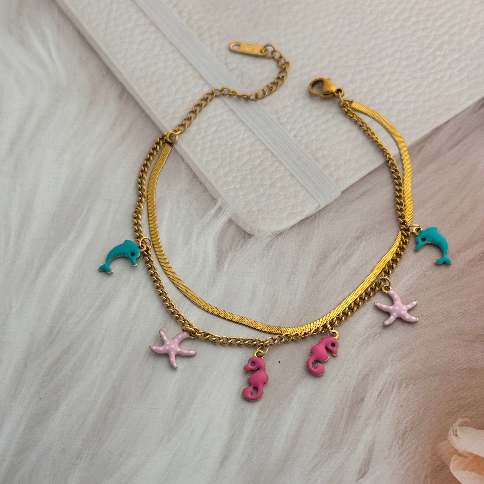Gold bracelet with colorful charms on a light wooden surface