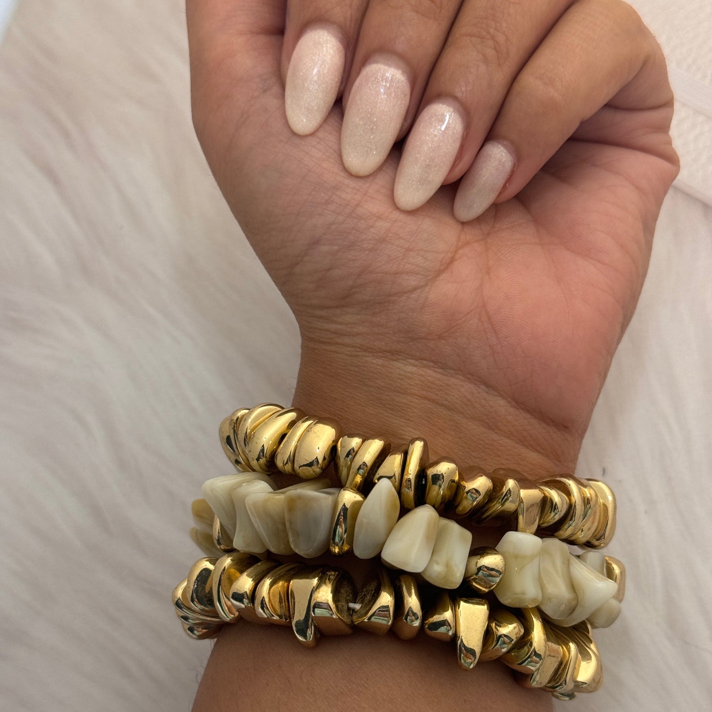 Hand wearing two gold and bone inlay bracelets on a neutral background