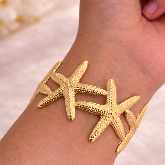 Gold starfish bracelet on a wrist with a soft background