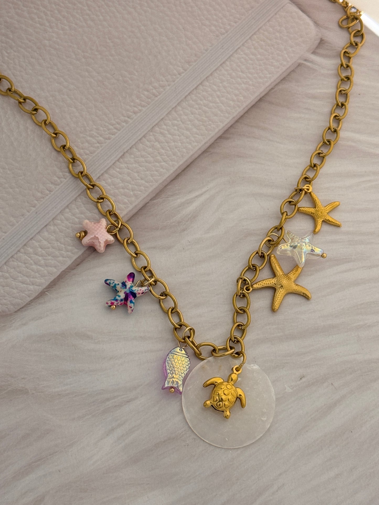 Gold chain bracelet with various charms on a textured surface