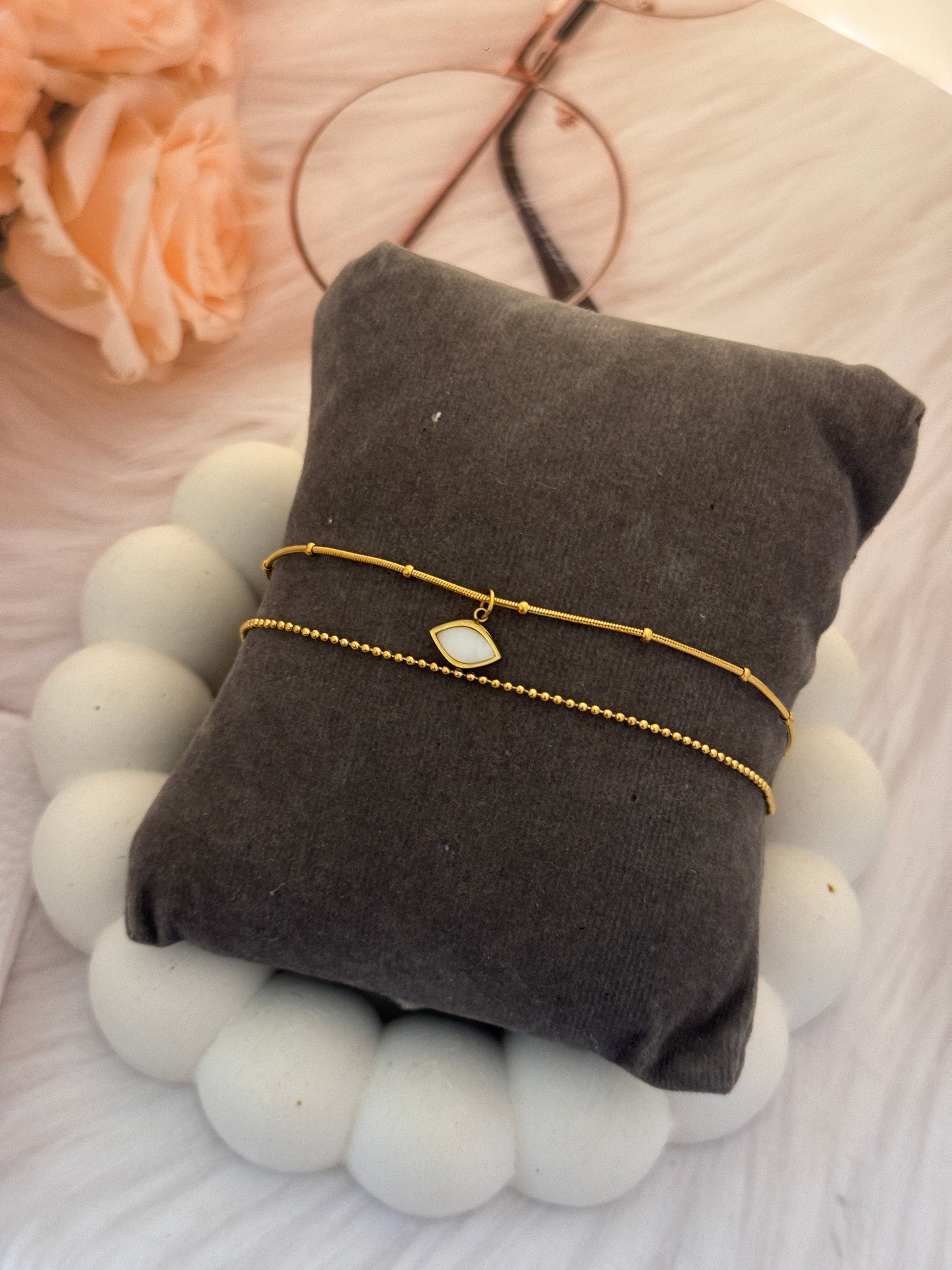 Gold bracelet on a gray cushion with white balls and flowers in the background