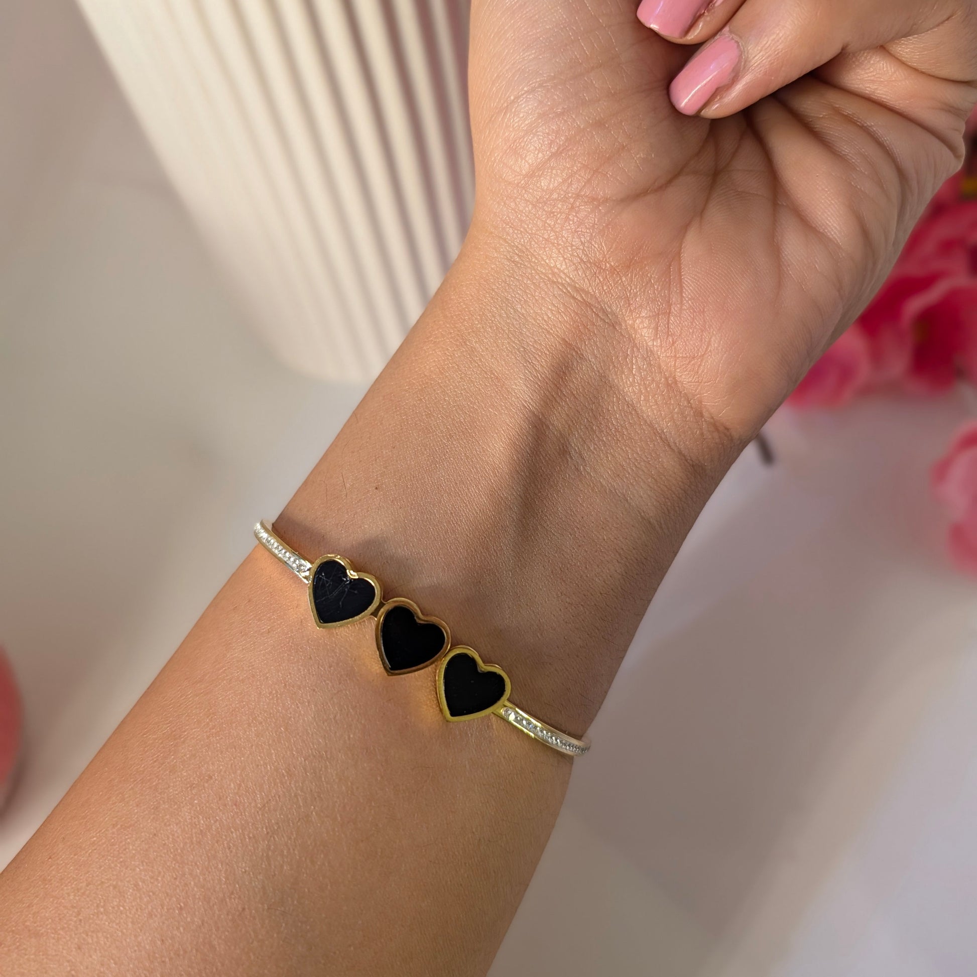 Gold bracelet with black heart charms on a wrist against a blurred background