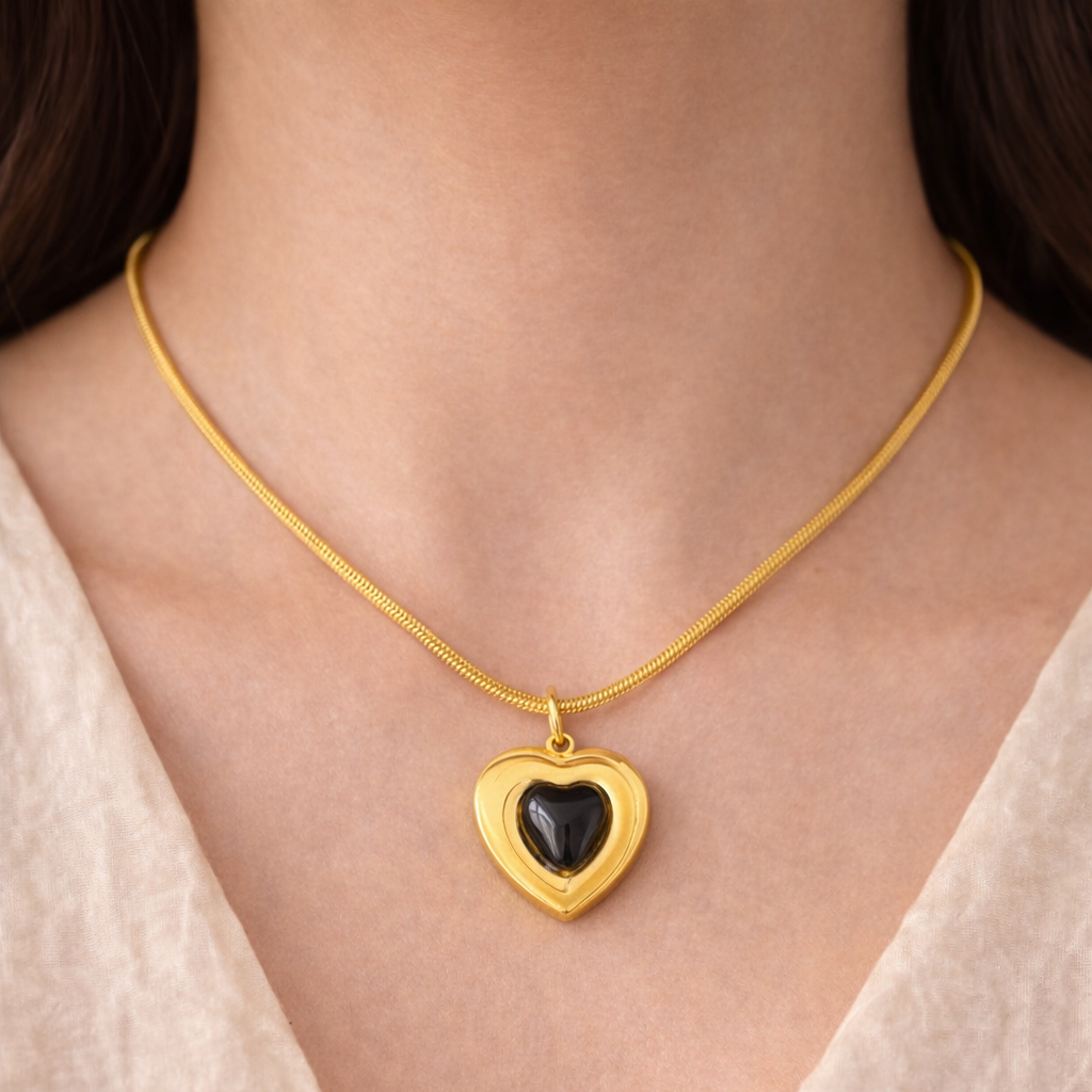 Gold necklace with a heart-shaped pendant on a person wearing a light-colored top.