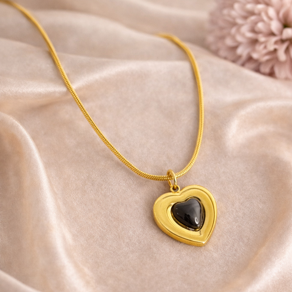 Gold heart-shaped necklace with a black stone on a beige fabric background