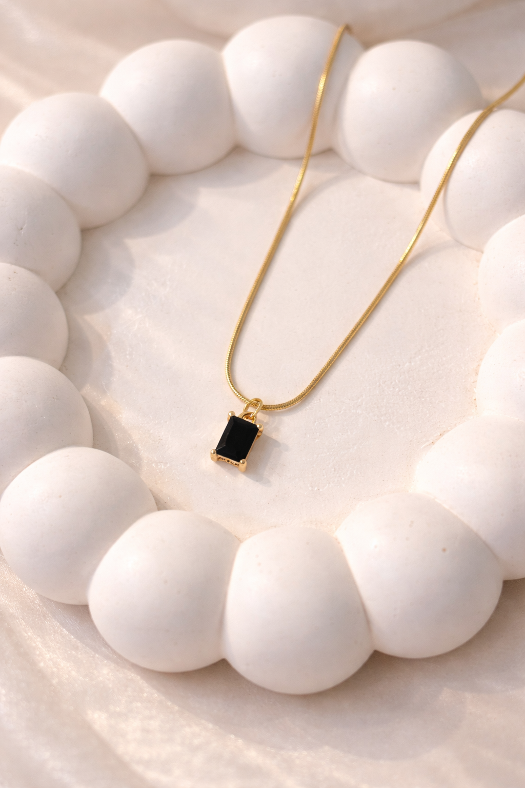 Gold necklace with a black pendant on a white stone surface