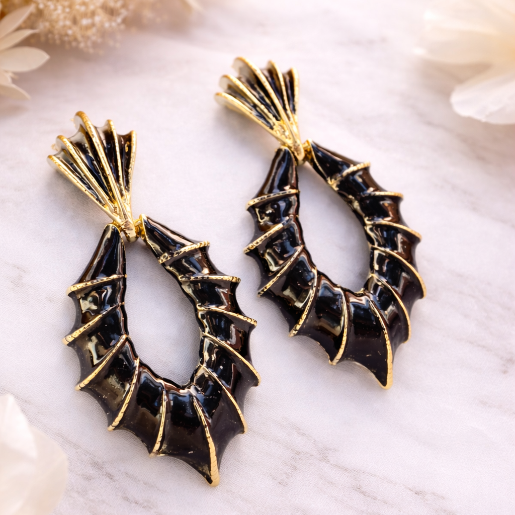 Black bat-shaped earrings with gold accents on a white surface.