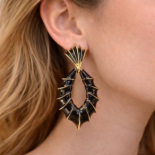 Black and gold earrings worn by a person with blonde hair.