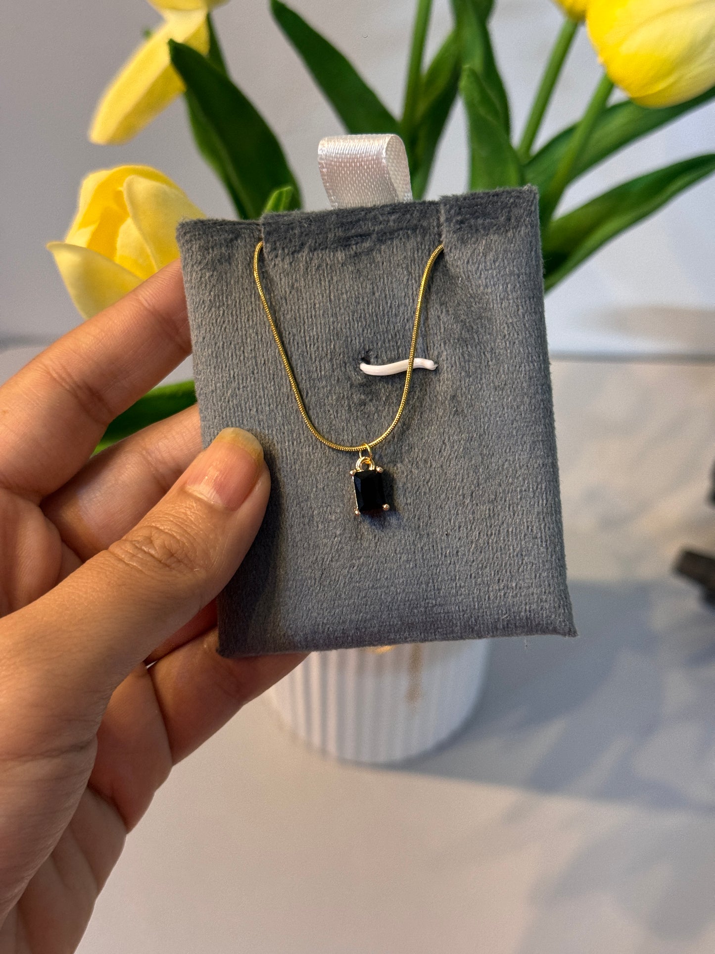 Hand holding a gold earring on a gray display card with yellow tulips in the background