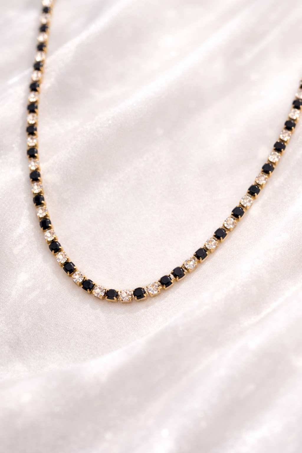 Necklace with black and clear gemstones on a white satin background