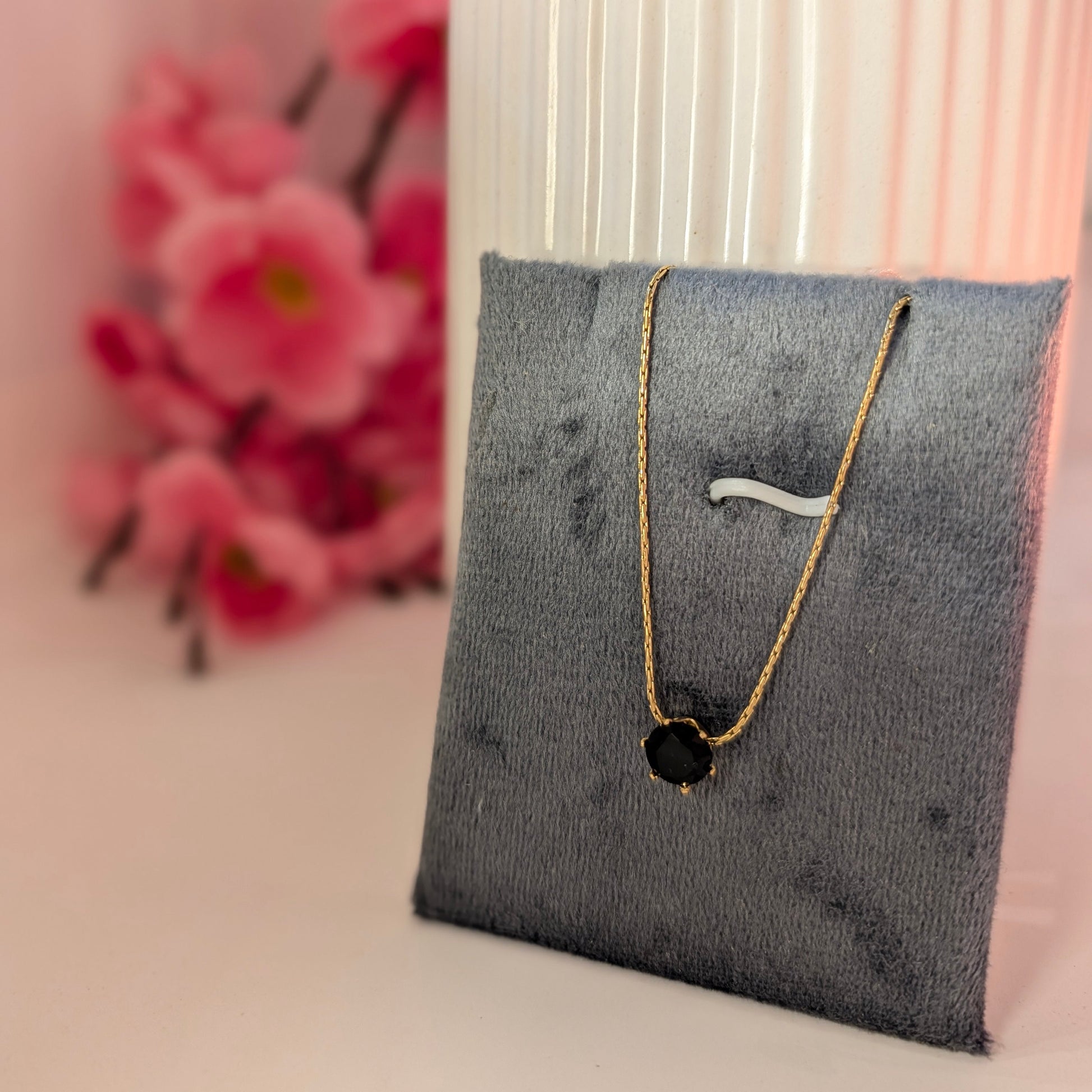 Necklace with black pendant on a gray stand with pink flowers in the background