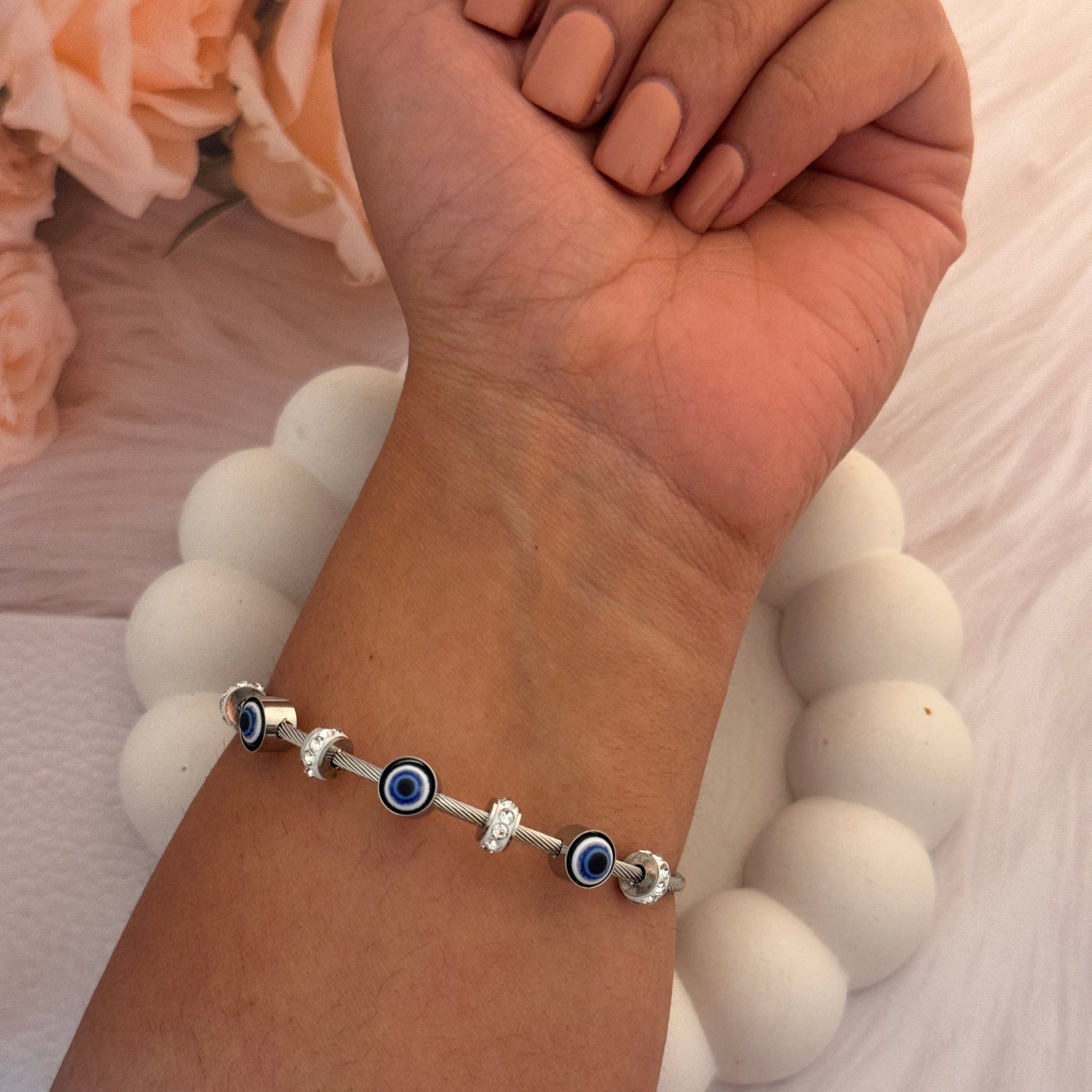 Hand wearing a bracelet with blue evil eye beads on a white background