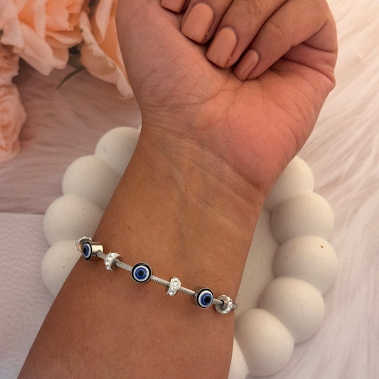 Hand wearing a bracelet with blue evil eye beads on a white background
