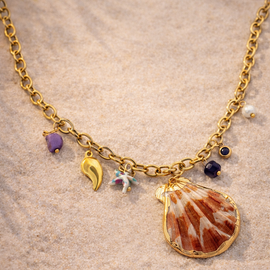 Gold necklace with shell charm on a sandy background