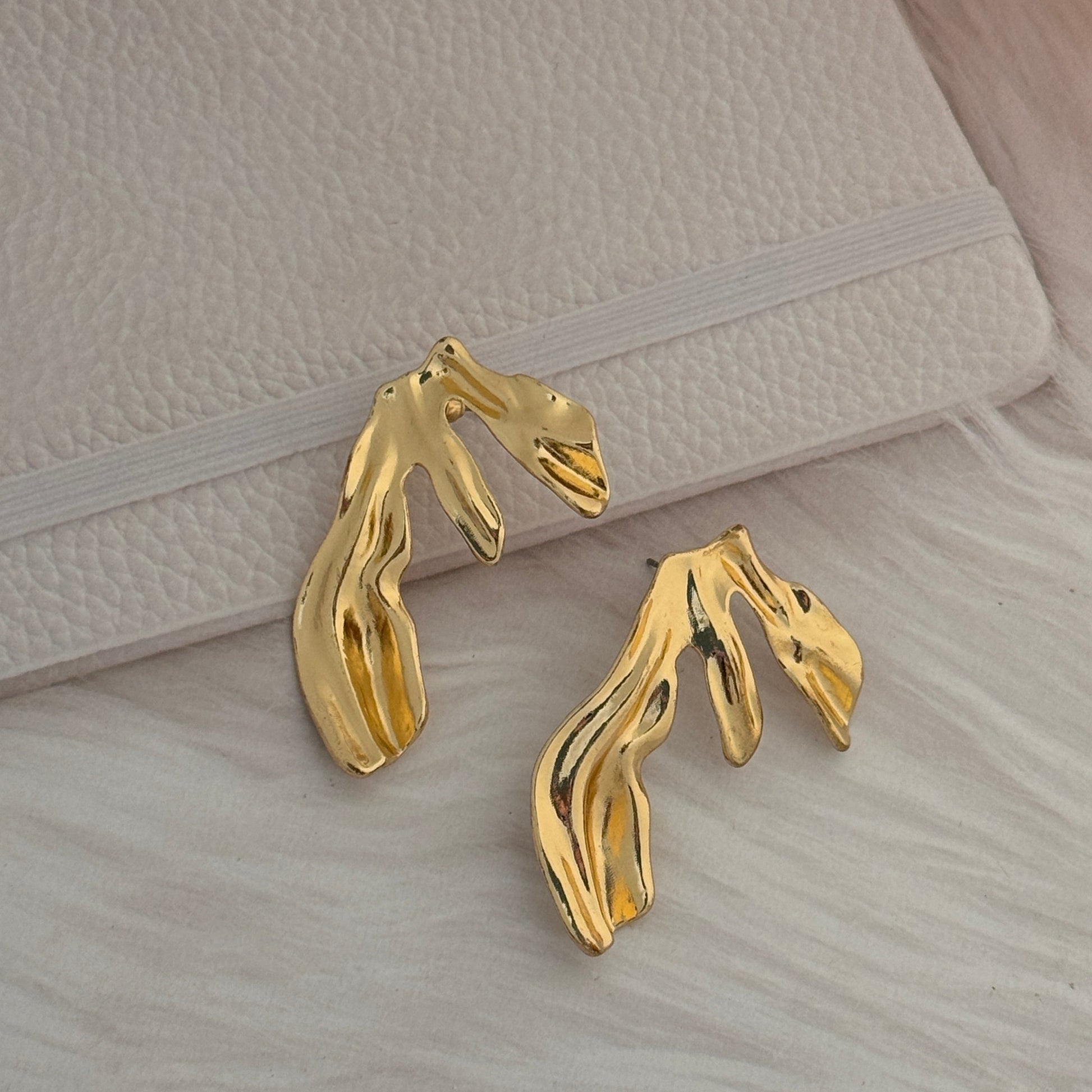 Gold abstract earrings on a textured surface