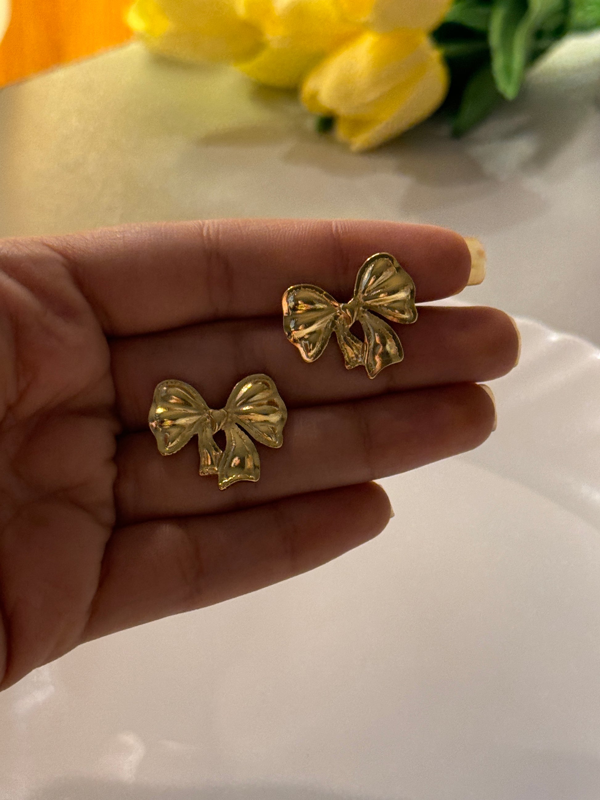 Gold bow-shaped earrings held in a hand with a blurred background