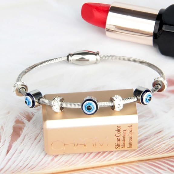 Bracelet with evil eye charms on a lipstick and Olay product, on a textured surface