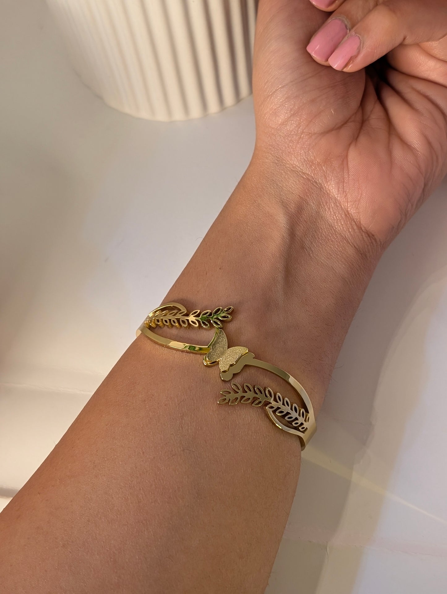 Gold bracelet with leaf and butterfly design on a wrist against a neutral background