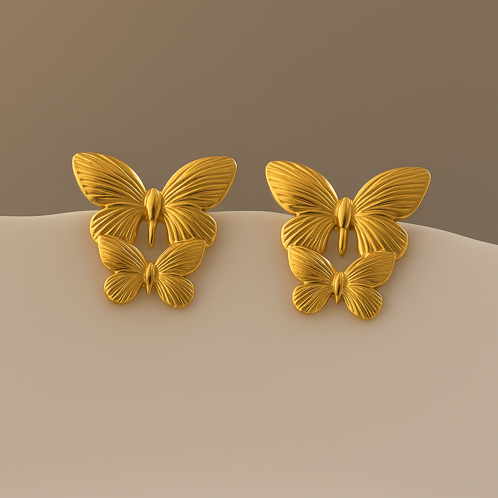 Pair of gold butterfly earrings on a beige surface with a brown background