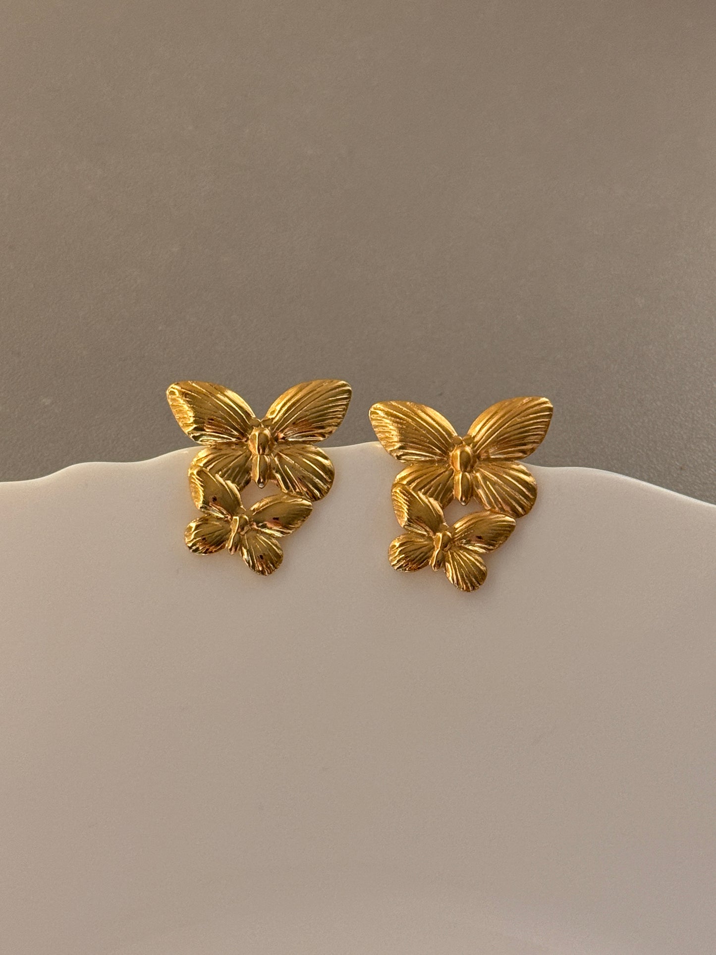 Gold floral earrings on a mannequin against a neutral background